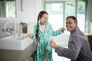 Smiling father and daughter brushing teeth in bathroom