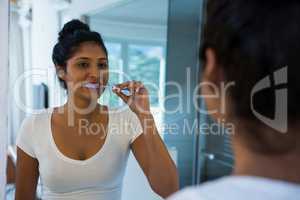 Woman brushing teeth with reflection on mirror