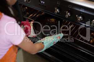 Cropped image of girl keeping container with cake in oven