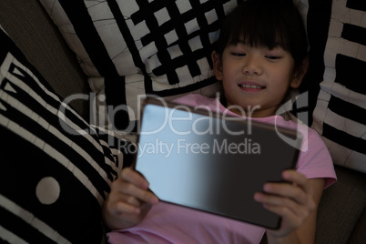 Girl using digital tablet while lying down on sofa