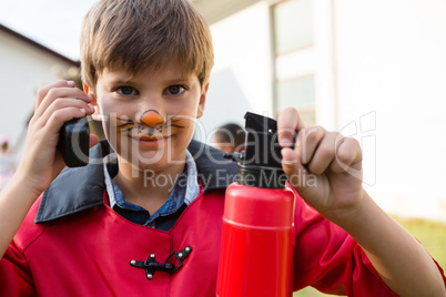 Portrait of boy with face paint using walkie talkie while holding fire extinguisher