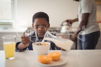 Boy pouring milk into breakfast cereals bowl in kitchen