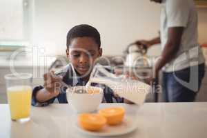 Boy pouring milk into breakfast cereals bowl in kitchen