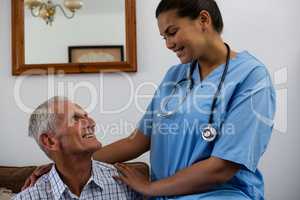 Smiling female doctor consoling senior man sitting on sofa