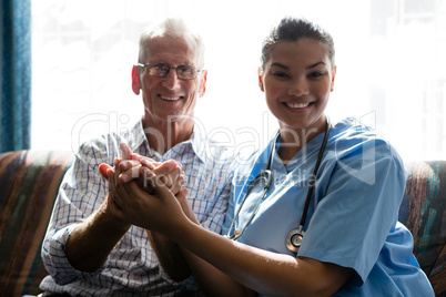 Portrait of senior man and female doctor holding hands in nursing home