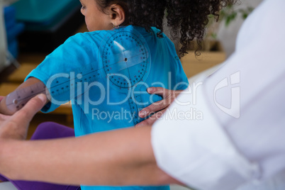 Physiotherapist examining girl patients back with goniometer
