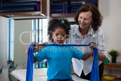 Physiotherapist assisting girl patient in performing stretching exercise from resistance band