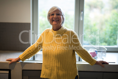 Smiling senior woman standing near kitchen worktop