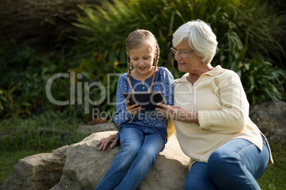 Smiling granddaughter and grandmother using digital tablet in garden