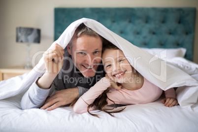 Smiling father and daughter lying on bed in bedroom