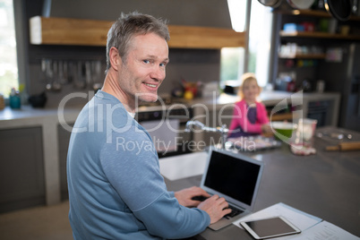 Man using his laptop while daughter preparing food in the kitchen