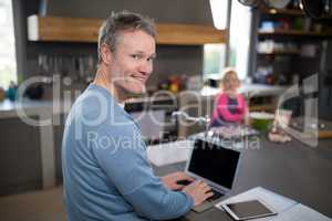 Man using his laptop while daughter preparing food in the kitchen