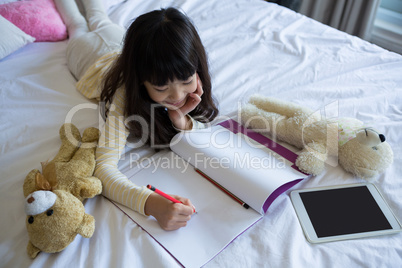 Girl with toys writing in book on bed