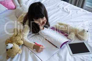 Girl with toys writing in book on bed