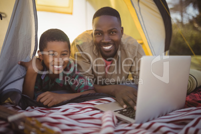 Smiling father and son using laptop in tent