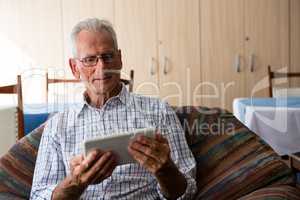 Senior man using tablet computer while sitting on armchair