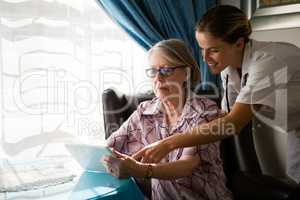 Female doctor assisting woman in using digital tablet