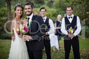 Wedding couple standing with bouquet of flowers in garden