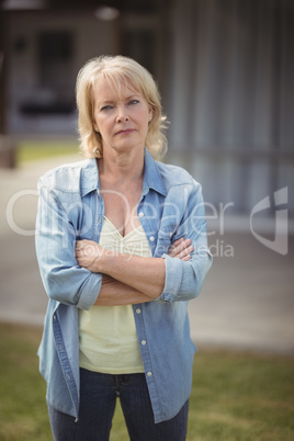 Senior woman standing with arms crossed outside her house