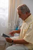 Side view of senior man using digital tablet while sitting on bed