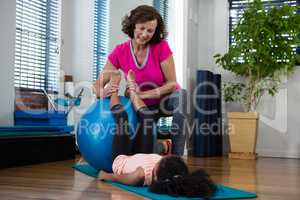 Female physiotherapist helping girl patient in performing stretching  exercise on exercise mat