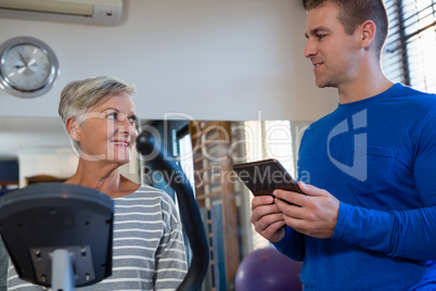 Physiotherapist interacting with senior woman while exercising on exercise bike