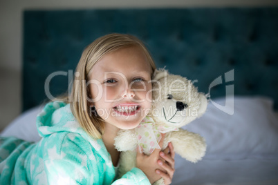 Smiling girl holding teddy bear on bed in bedroom