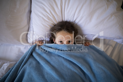 Girl covering her face under the blanket while lying on bed
