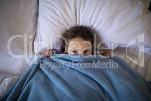 Girl covering her face under the blanket while lying on bed