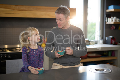 Little girl and father looking at each other while eating fruits from a bowl