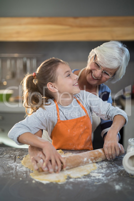 Grandmother and granddaughter looking at each other while flattening dough