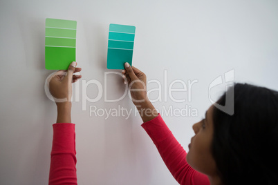 Young woman holding color swatches by wall