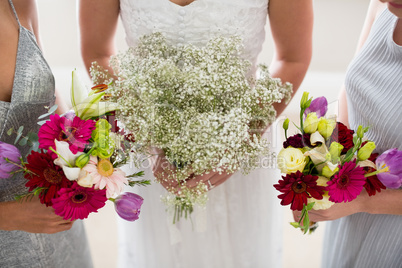 Mid section of bride and bridesmaids standing with bouquet