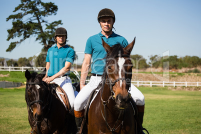 Two male jockeys riding horse in the ranch