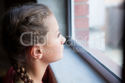 Thoughtful teenage girl looking through window