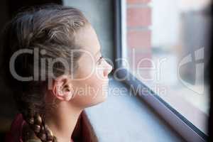 Thoughtful teenage girl looking through window