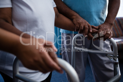 Midsection of friend assisting woman in walking with walker