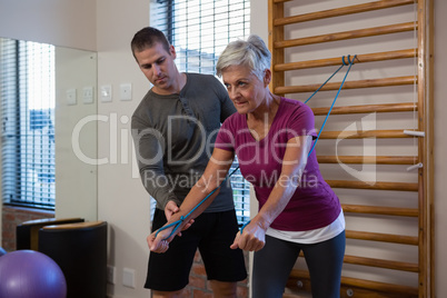 Male physiotherapist helping patient in performing exercise with resistance band