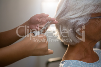 Cropped hands of beautician cutting hair of senior woman