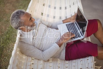 Senior man using laptop while relaxing on hammock