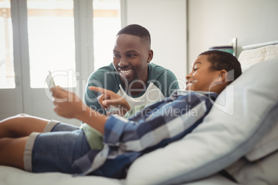 Son showing digital tablet to his father in bedroom