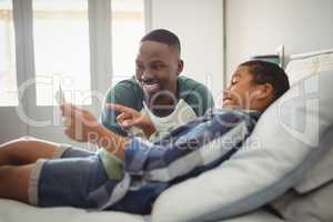 Son showing digital tablet to his father in bedroom