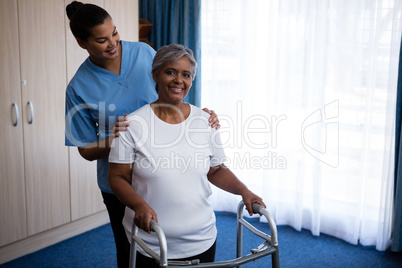 Nurse assisting woman in walking with walker at nursing home