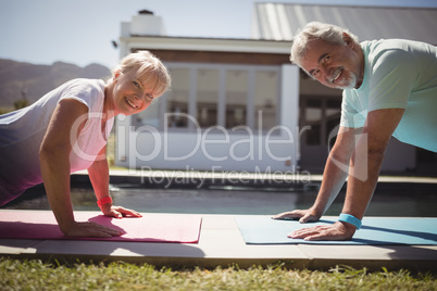 Smiling senior couple doing push-up near swimming pool