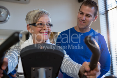 Physiotherapist assisting senior woman in performing exercise on exercise bike