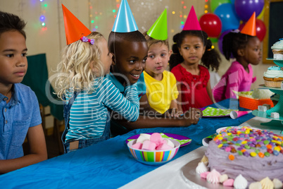 Girl whispering to boy at table