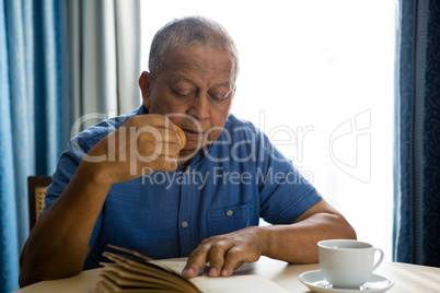 Senior man eating food while reading book in nursing home