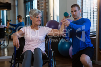 Male physiotherapist helping patient in performing exercise with dumbbell