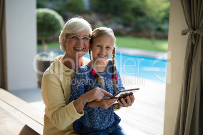 Granddaughter and grandmother using a digital tablet in the deck shade