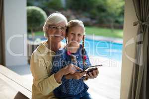 Granddaughter and grandmother using a digital tablet in the deck shade